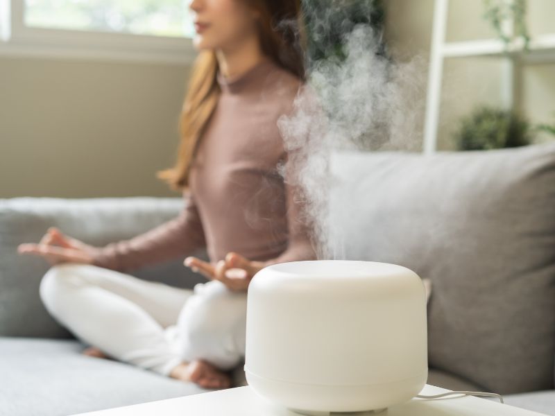 người phụ nữ mở máy khuếch tán tinh dầu và thiền